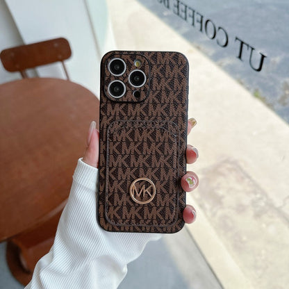 A black iPhone case with a repeating pattern and a gold MK logo in the center.